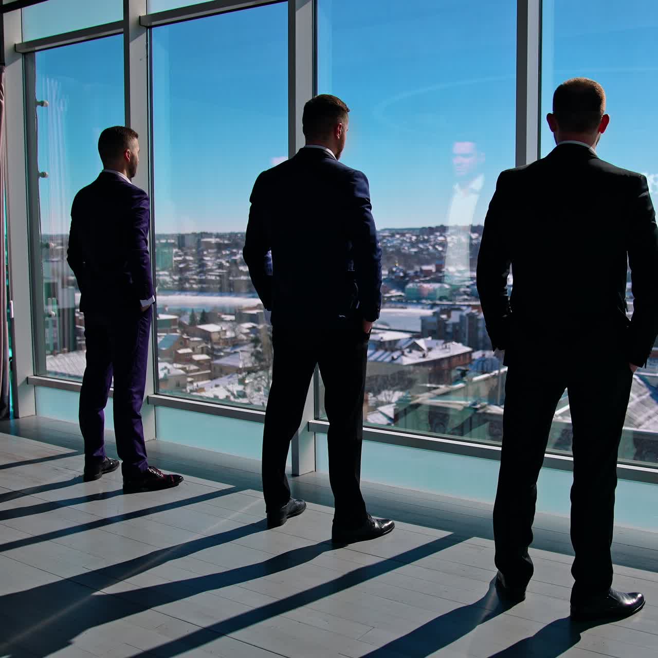 Elegant businessmen looking through office window. Back view of colleagues group rest at break. Business people in suits have a conversation near window