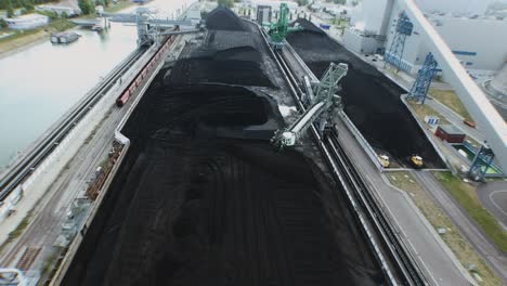 Drone-flight-over-a-coal-field-with-yellow-digger-alongside-of-a-river-in-western-Europe-at-a-power-plant