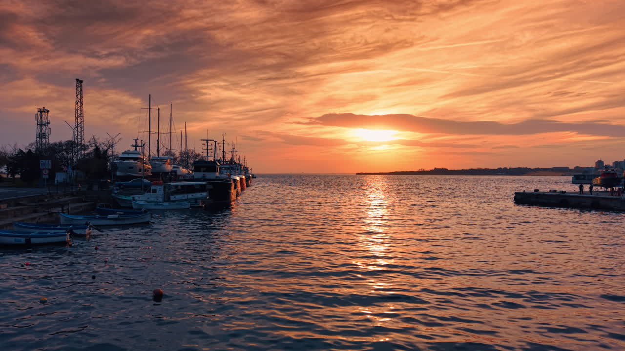 Il sole al tramonto si riflette sulla superficie frastagliata del paesaggio marino. Il cielo arancione è coperto di nuvole al tramonto. Riprese al molo con barche.