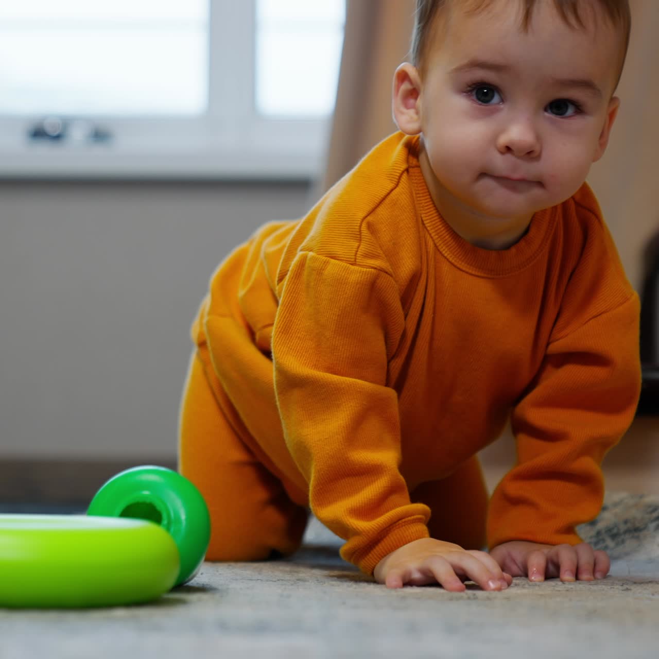 Beautiful dark-eyed Caucasian boy stands on all four on the floor. Kid smiles and crawls up closer to camera