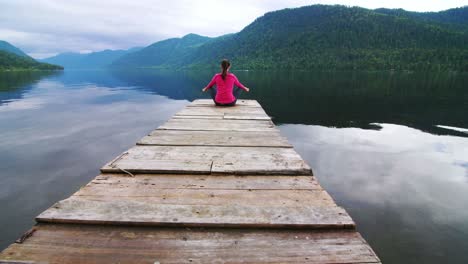 woman meditating on a wooden dock by a lake