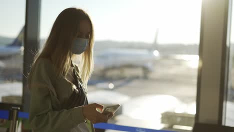 blonde woman in medical mask uses phone walking through airport terminal