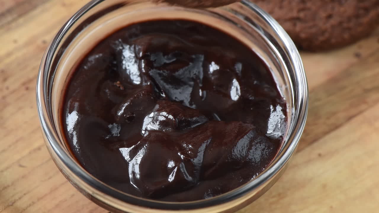 Close up of a woman dipping a cookie in a chocolate paste on a wooden tray