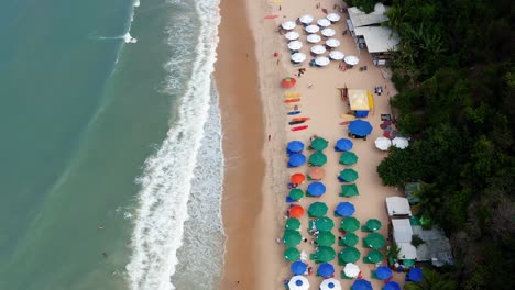 Wunderschöne-Luftdrohne-Vogelperspektive-Vorbeiflug-Des-Tropischen-Strandes-Praia-Do-Madeira-Mit-Bunten-Strandschirmen-Und-Touristen,-Die-In-Der-Nähe-Der-Berühmten-Stadt-Pipa-Im-Norden-Brasiliens-Schwimmen-Und-Surfen