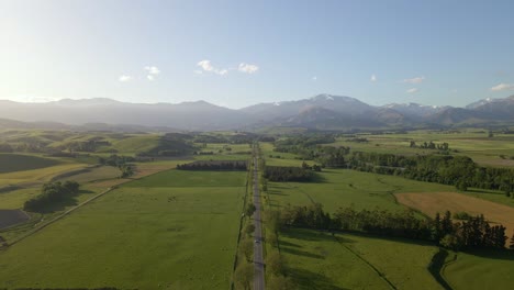 aerial: perfectly straight countryside highway leading towards majestic mountain range in warm evening sunshine