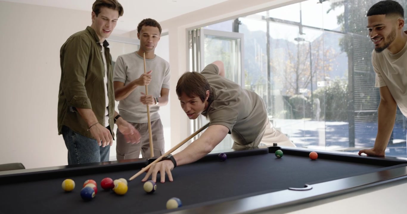 Diverse male friends playing pool by doors, cheering after shot, breaking rack, scattering balls