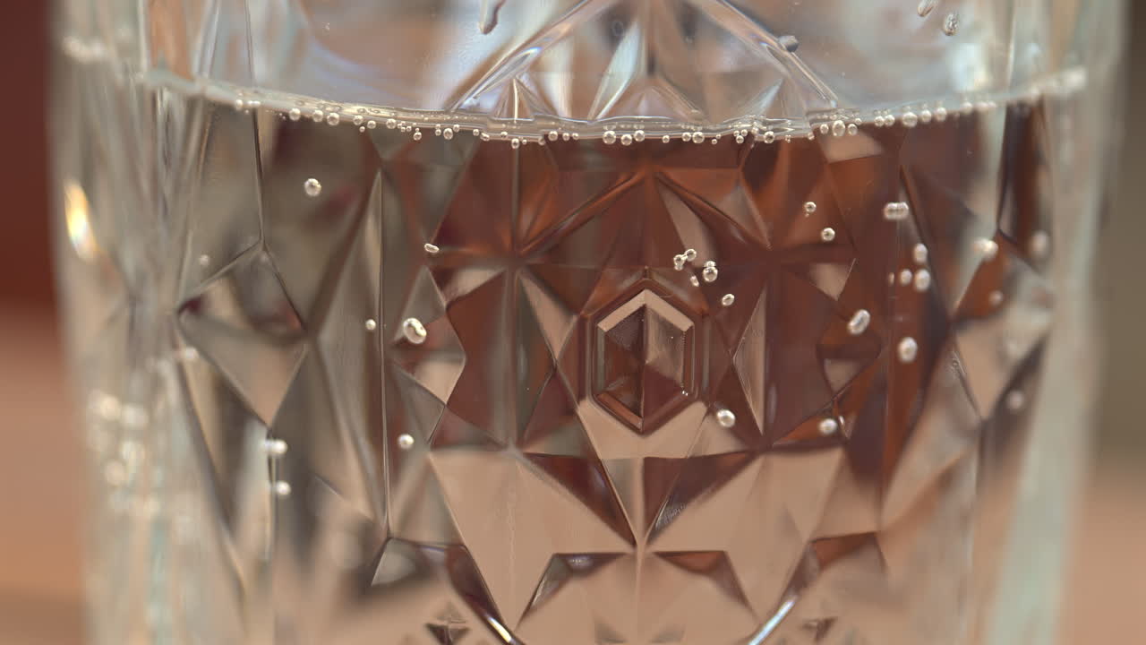 Close up of bubbles moving up in a glass of sparkling water on a wooden table