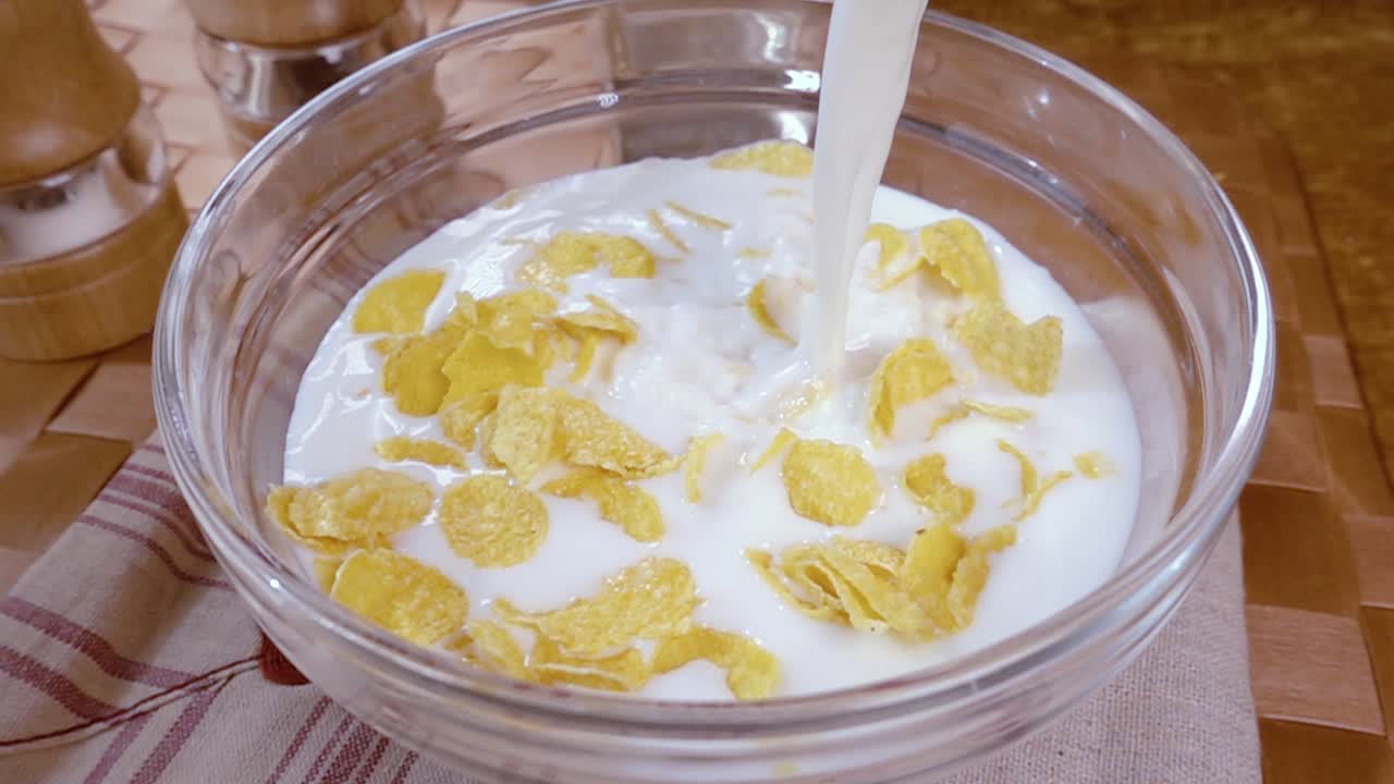 Knusprige gelbe Cornflakes in die Schale für ein köstliches Frühstück mit Milch am Morgen. Zeitlupe mit rotierender Kamerafahrt