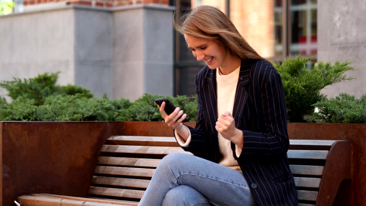 Business Woman Celebrating Success while Using Smartphone