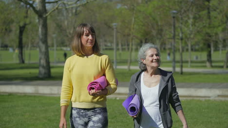 front view of women in park holding yoga mat in hands, talking