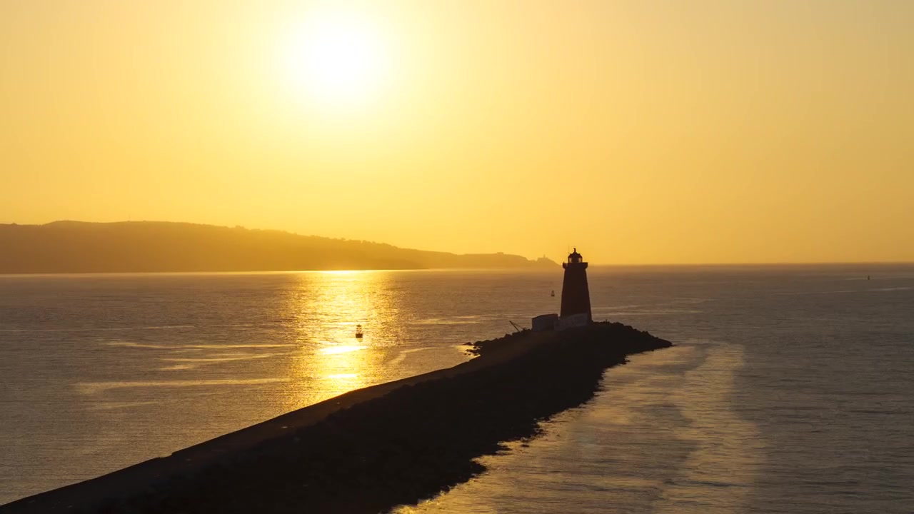 O Farol de Poolbeg ergue-se em seu longo quebra-mar enquanto o sol baixo brilha sobre o mar calmo em um sobrevoo aéreo lento