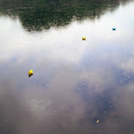 three colorful paper ships on water under the rain. handmade origami ships are floating on the water surface during the rain outdoors. top view.