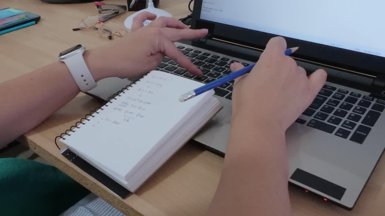 Hands organizing thoughts and plans, writing in a notebook alongside a laptop.