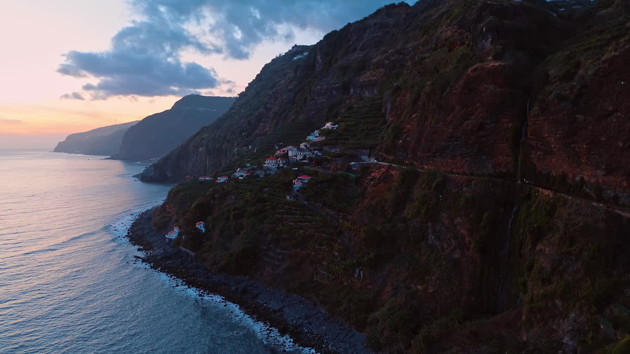 Cozy village locating on the slope of the rock. Mountainous shore of Madeira, Portugal at the waterscape of the Atlantic Ocean. Aerial view.