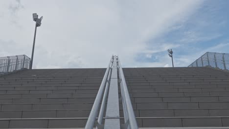 a low-angle shot of a wide concrete staircase with metal handrails leading up to a cloudy sky