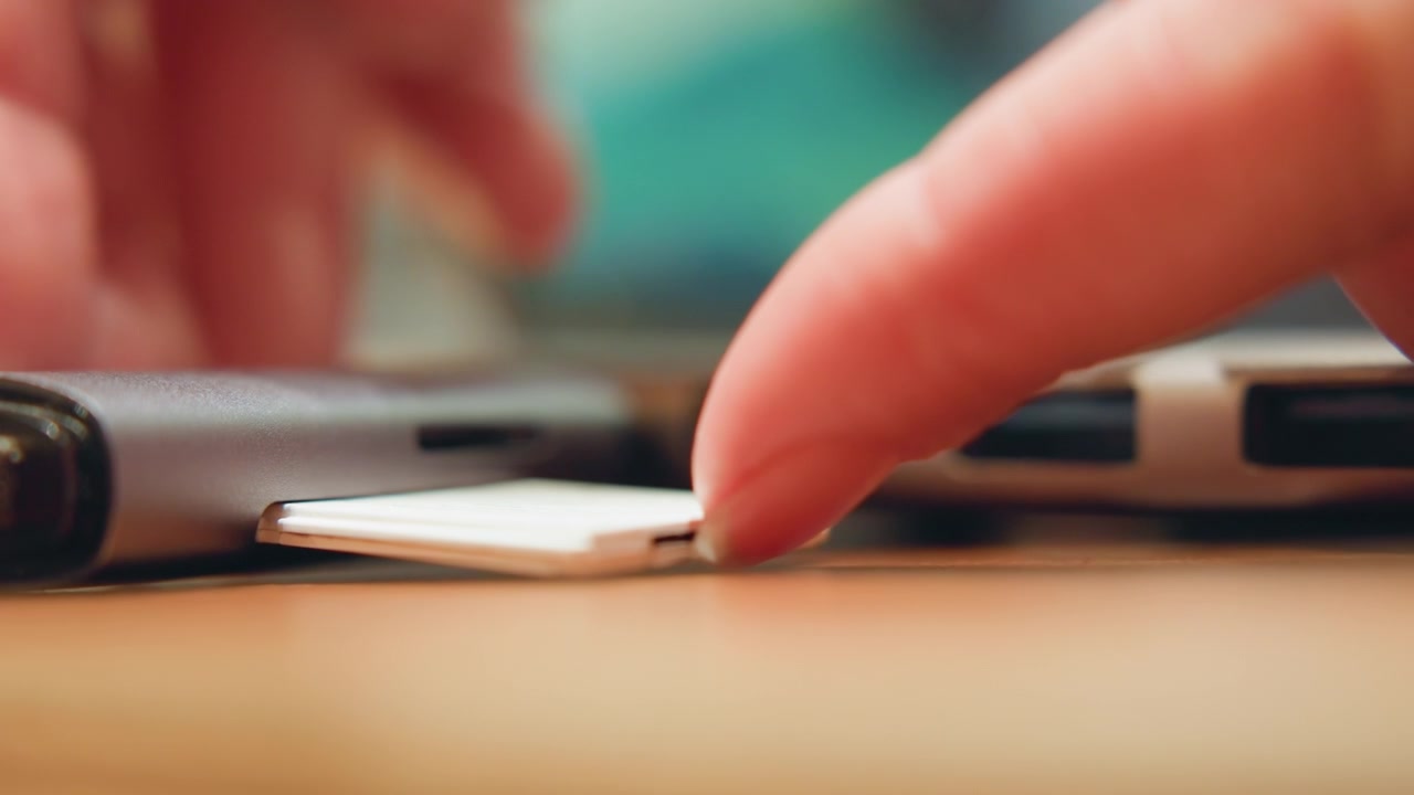 Primo piano di una scheda SD inserita nello slot di un laptop, con il polpastrello che la fa scorrere e la allinea con precisione, scena di trasferimento multimediale per il backup di foto e video, superficie calda della scrivania e un momento di flusso di lavoro moderno.