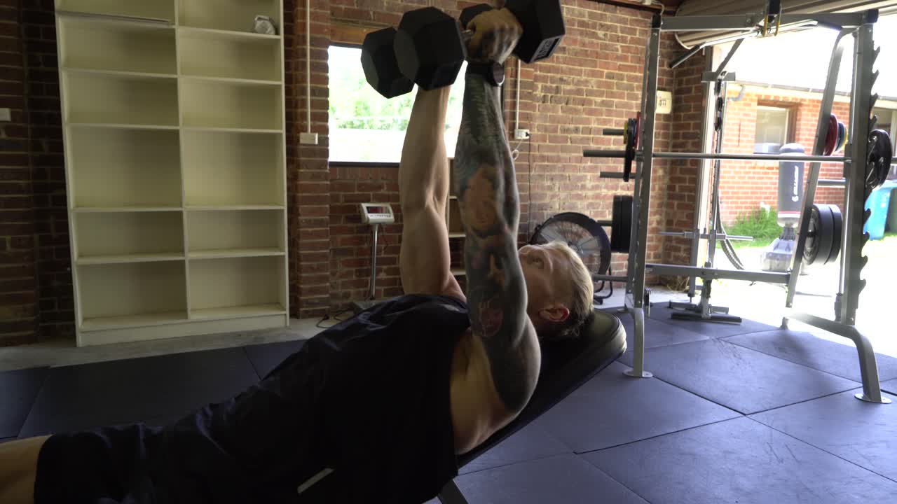 Tattooed man in home gym doing incline chest flys