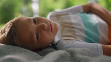 portrait of tranquil boy lying on blanket closeup. blond kid looking on camera.