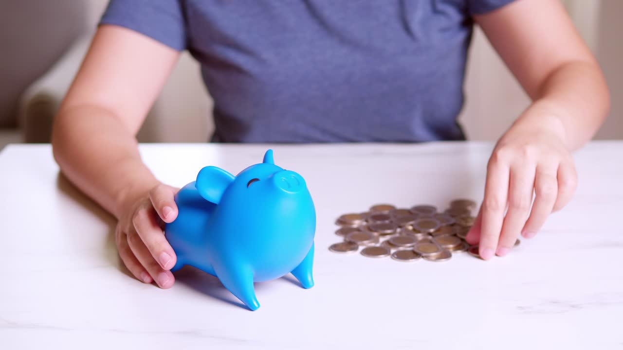 Hands of a woman putting money coin into blue piggy bank with blank metaphor separate kind of money for spend and saving