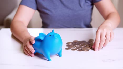 manos de una mujer poniendo dinero en una alcancía azul con una metáfora en blanco tipo de dinero separado para gastar y ahorrar