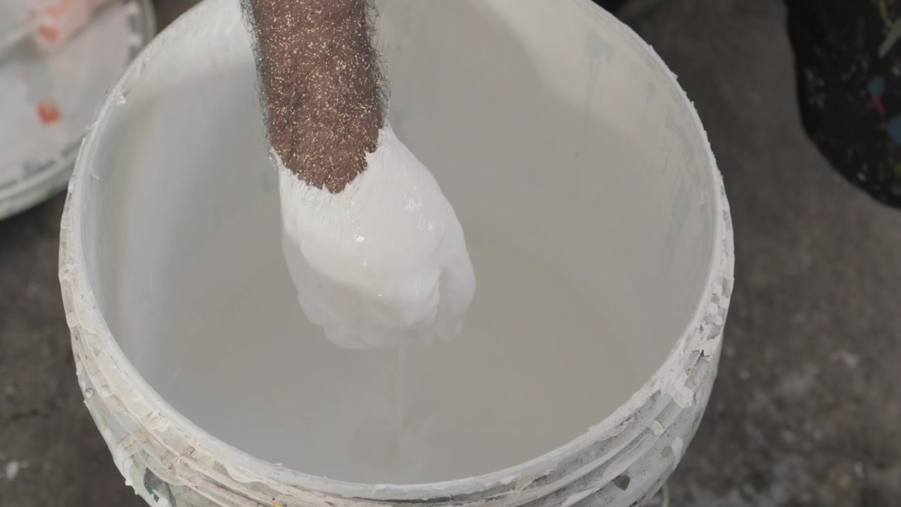 Werknemer bereidt een aangepaste muurkleur voor door verf in een emmer te mengen, waardoor een unieke tint ontstaat voor schilder- en renovatieprojecten
