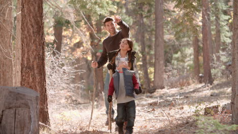 father walking in forest with two kids, picks up a pine cone