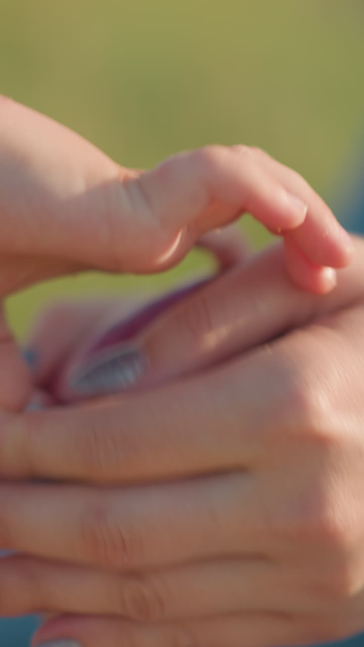 un primer plano de las manos de una mujer limpiando suavemente una manzana roja, preparándose para entregarla a un niño. el fondo es un campo de hierba verde borroso, destacando el cuidado simple en este momento tierno