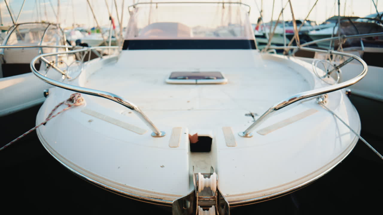 Vorderansicht eines weißen Motorbootbugs, der am Dock befestigt ist und Metallgeländer, Seile und nautische Details im weichen Tageslicht zeigt