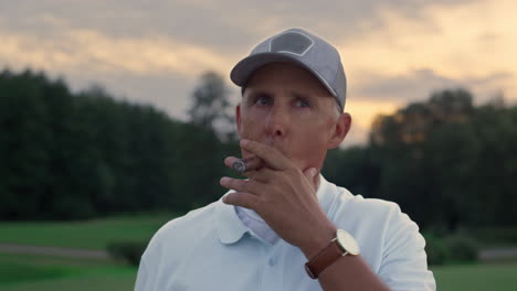 Relaxed-senior-smoking-cigar-on-golf-course.-Old-man-enjoy-rich-life-weekend.