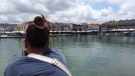 tourist girl taking panoramic picture of the rethimno’s venetian port with her smartphone in landscape position