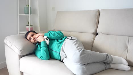 Frustrated man with toothache lays in sofa putting ice to the cheek