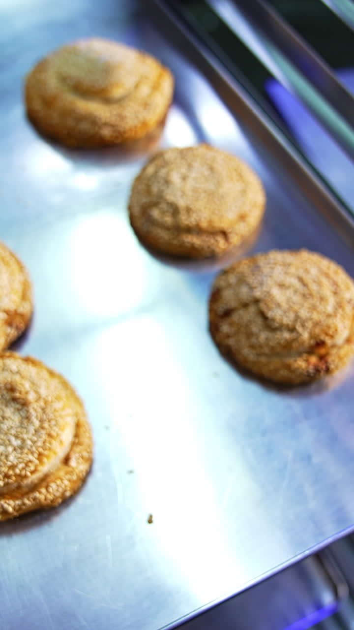 Sweet pastry manufacturing at bakery. Brown baked bagels and buns put on the baking sheet. Close up. Vertical video