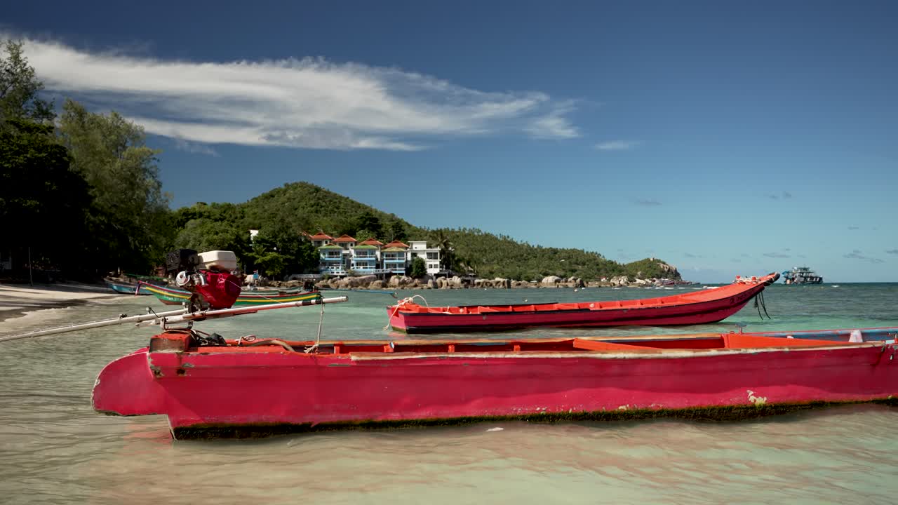 Red wooden boats peacefully moored in the shallow, clear waters of Koh Tao, Thailand, with lush green hills and blue sky in the background