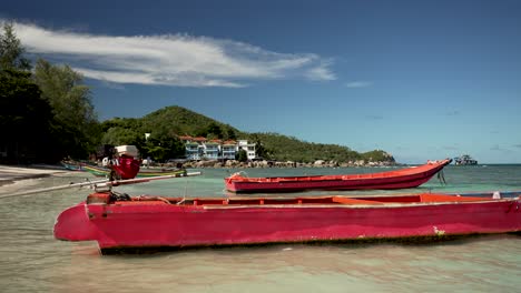 red wooden boats peacefully moored in the shallow, clear waters of koh tao, thailand, with lush green hills and blue sky in the background