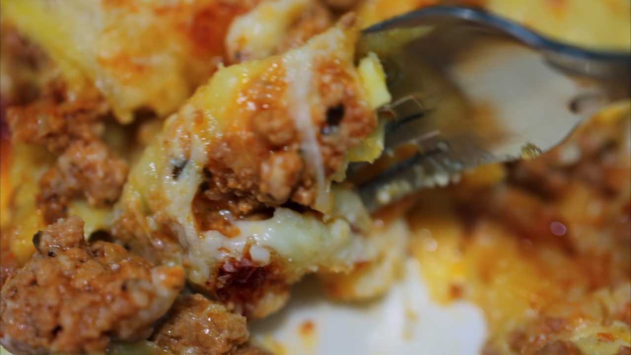 Close up of a fork picking up lasagna from a white plate