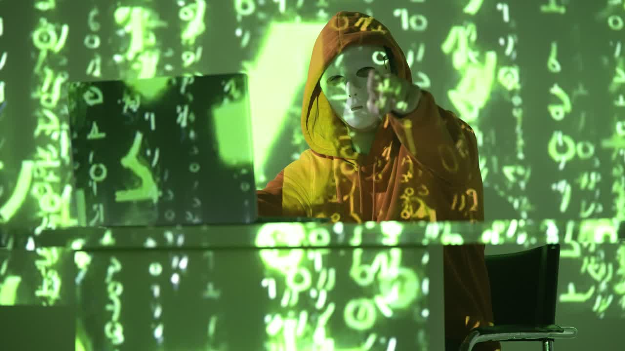 A masked hacker in an orange hoodie types in a dark room, immersed in cascading neon code, portraying themes of cybersecurity threats, data intrusion, and digital warfare