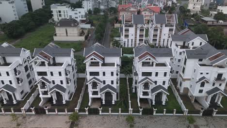 a newly constructed row of identical large white multi story villa styled houses along a suburban road