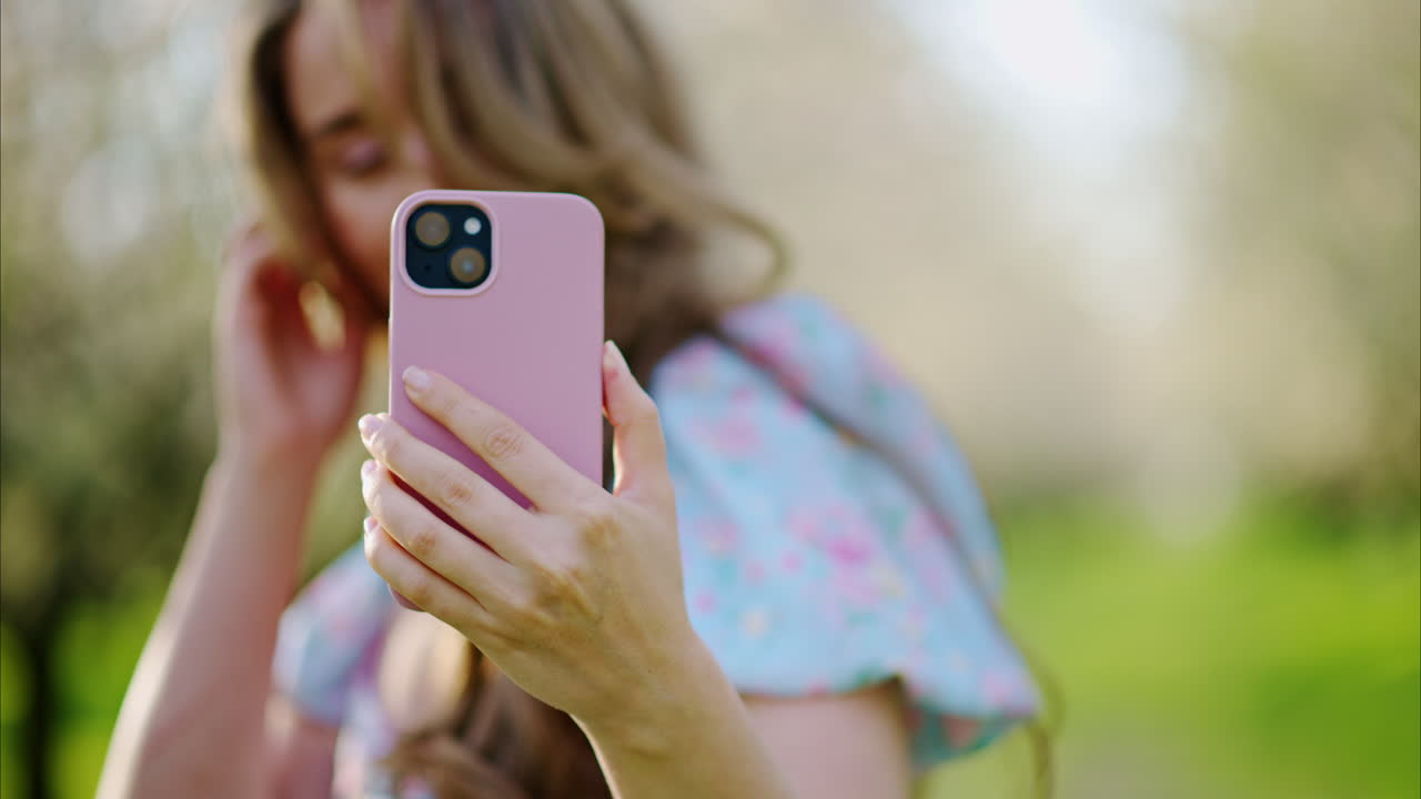 Brunette woman in a blue dress, taking pictures in a field of blooming almond trees