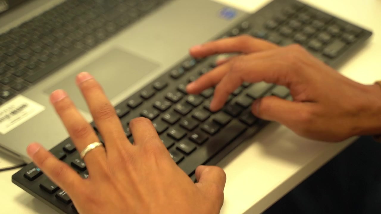Close up of hands typing on a computer keyboard at a desk