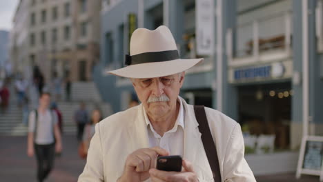 close up portrait of stylish elderly man tourist texting browsing using smarphone mobile technology in busy urban city wearing white suit