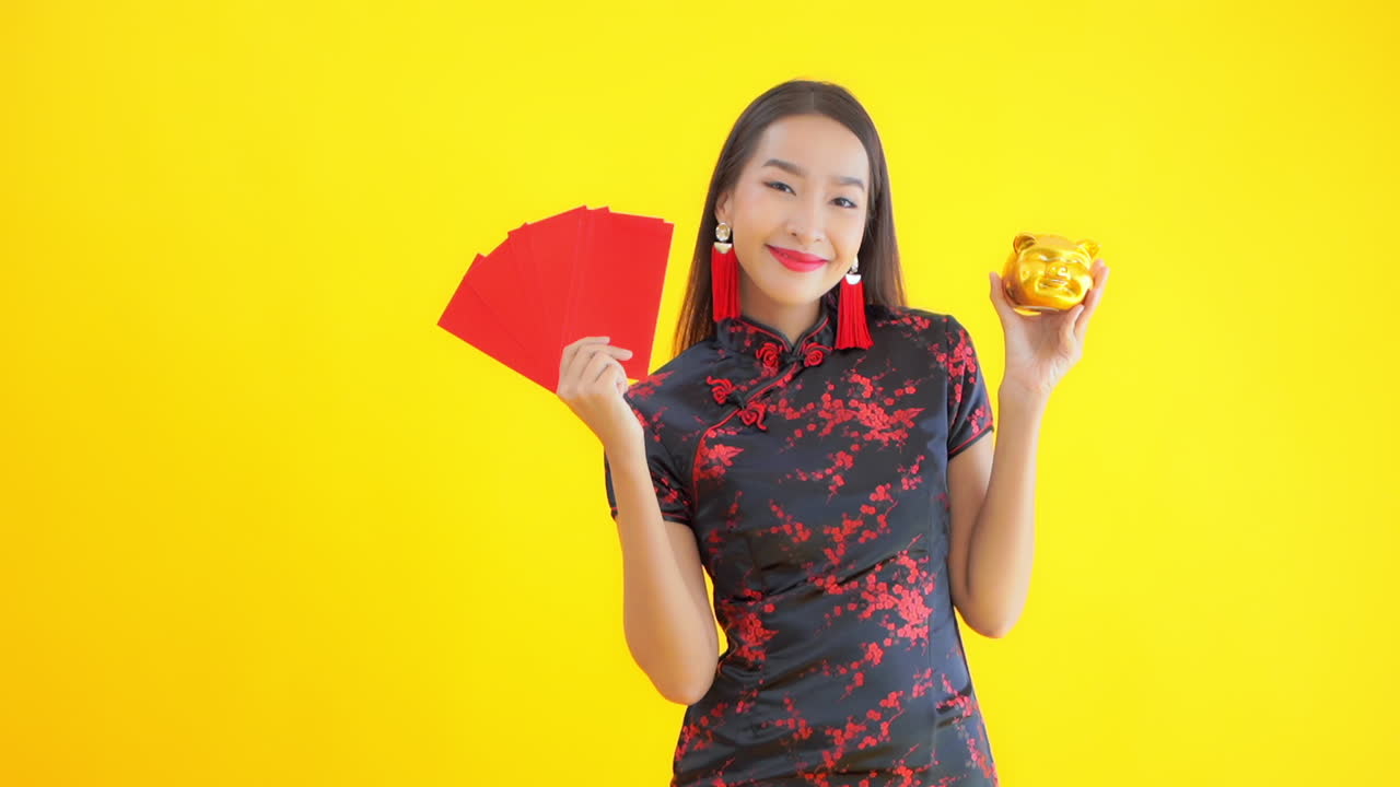 Asian woman in Chinese traditional costume holding stack of red envelopes with money and golden piggy bank. Chinese New Year
