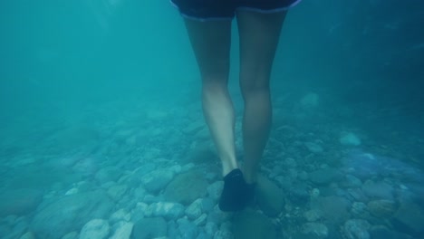 一位女人走在快速流动的河流的滑滑的岩石底部