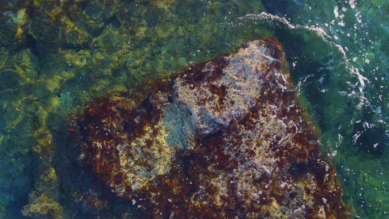 the interaction of waves against rocks underneath the unblemished, translucent water during a day filled with bright sunshine