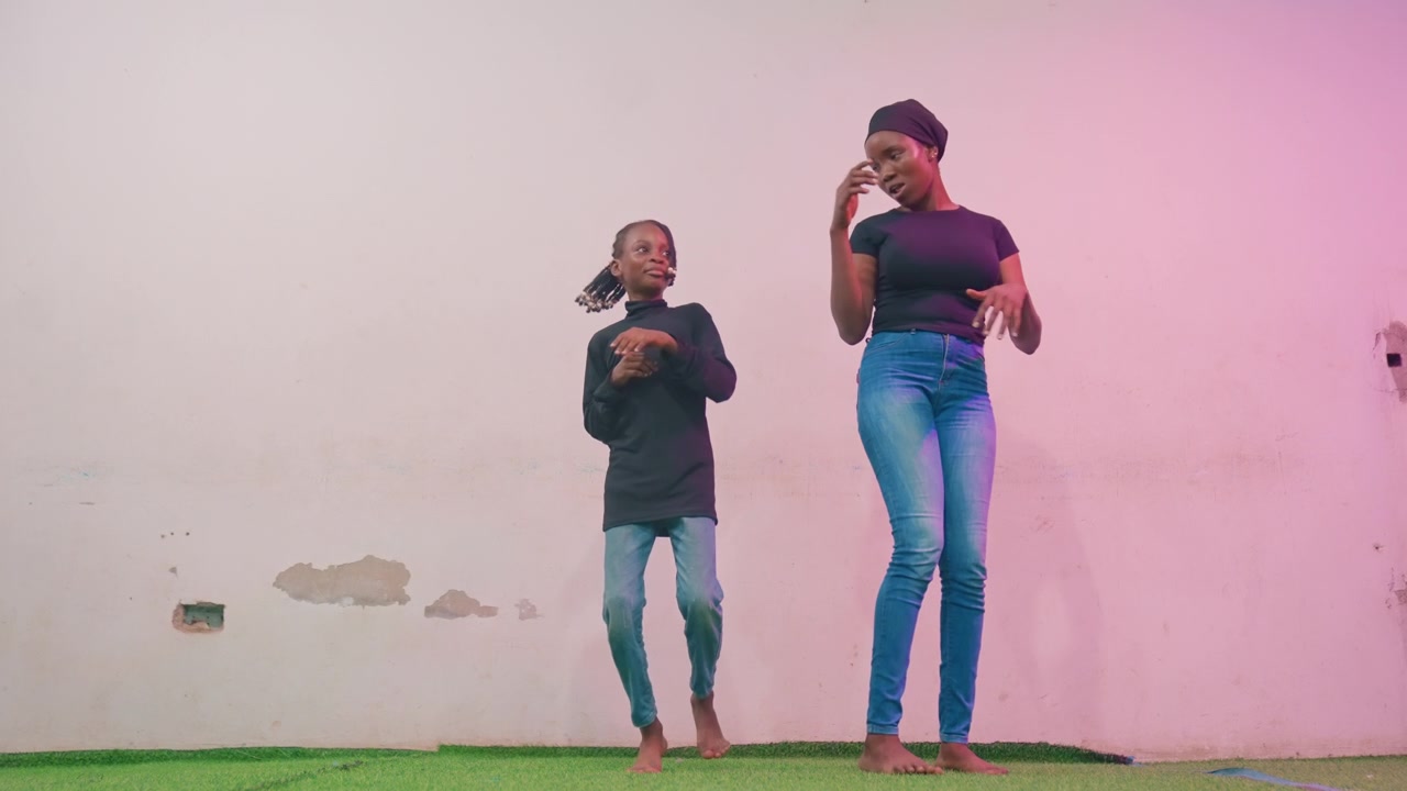 Joyful duet performance. Mother and child dance together. Lively duet between mother and youngster on grassy area. Upbeat performance of mother with child dancing on grass near colored wall