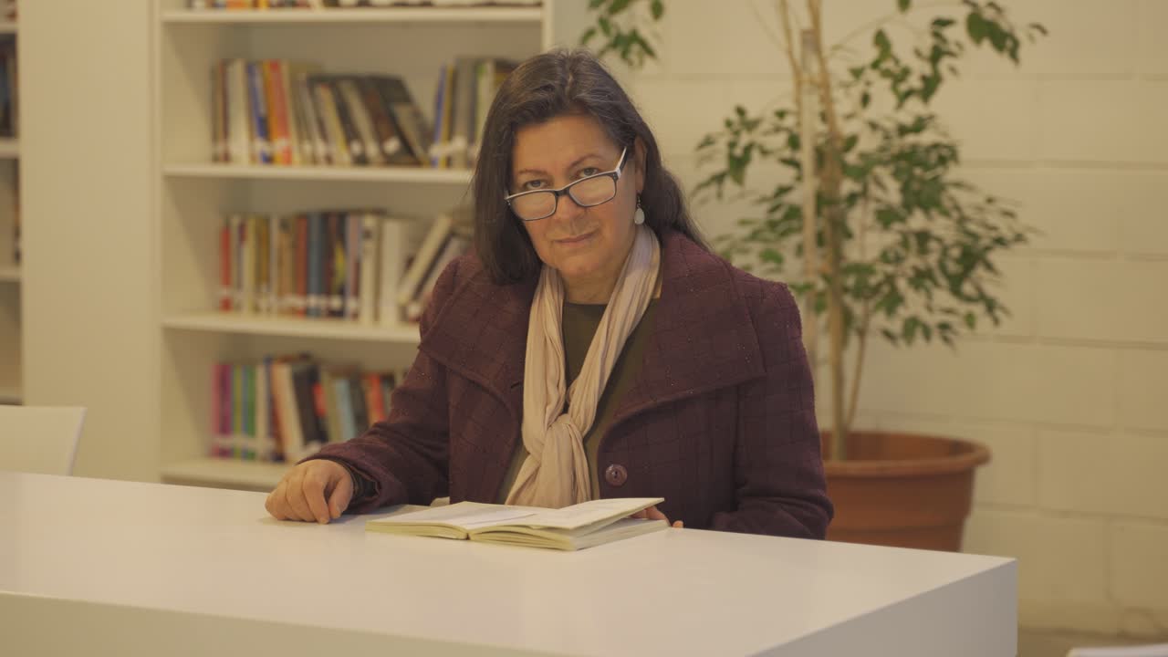 hermosa mujer de mediana edad sentada en la biblioteca sonríe mientras mira la cámara