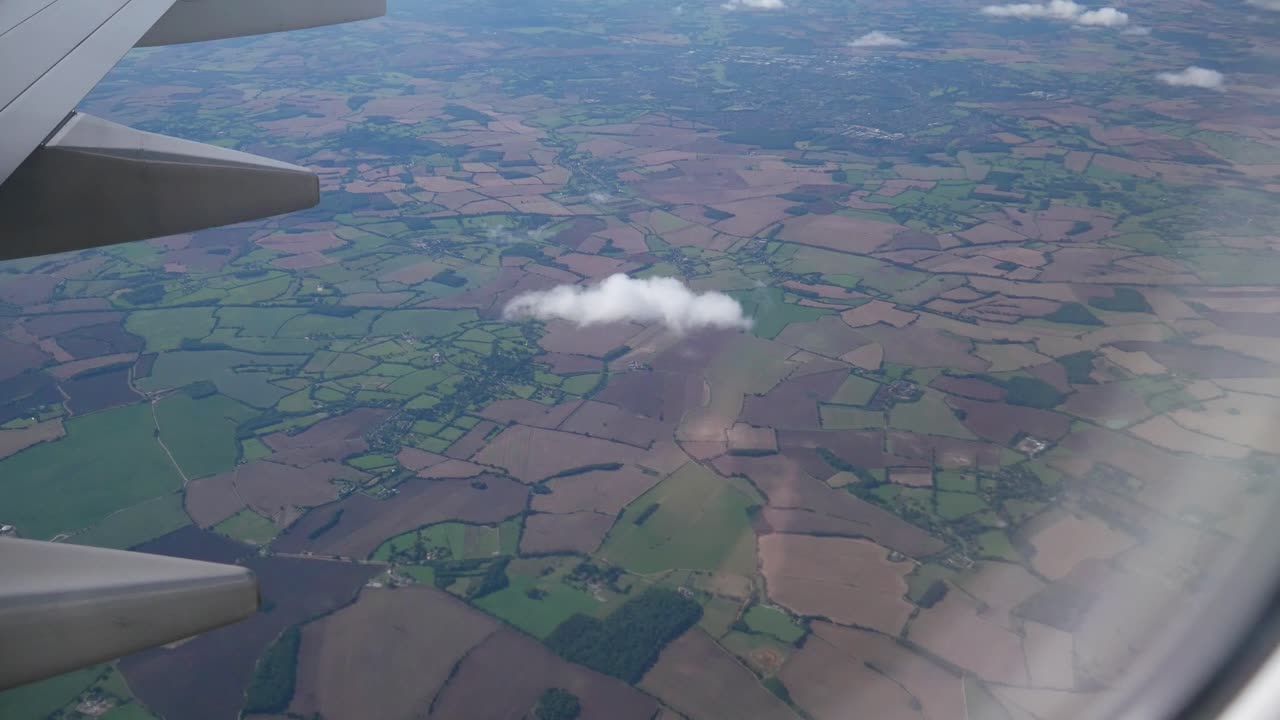 vista desde un avión de tierras de cultivo que pasan con pequeñas nubes.