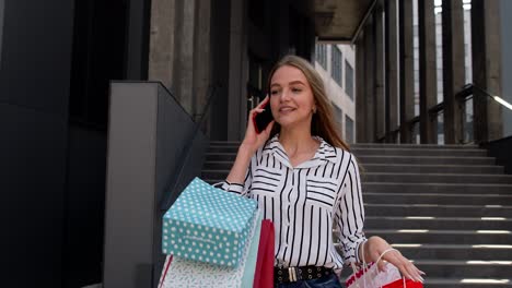 girl walking from mall with shopping bags and talking on mobile phone about sale on black friday