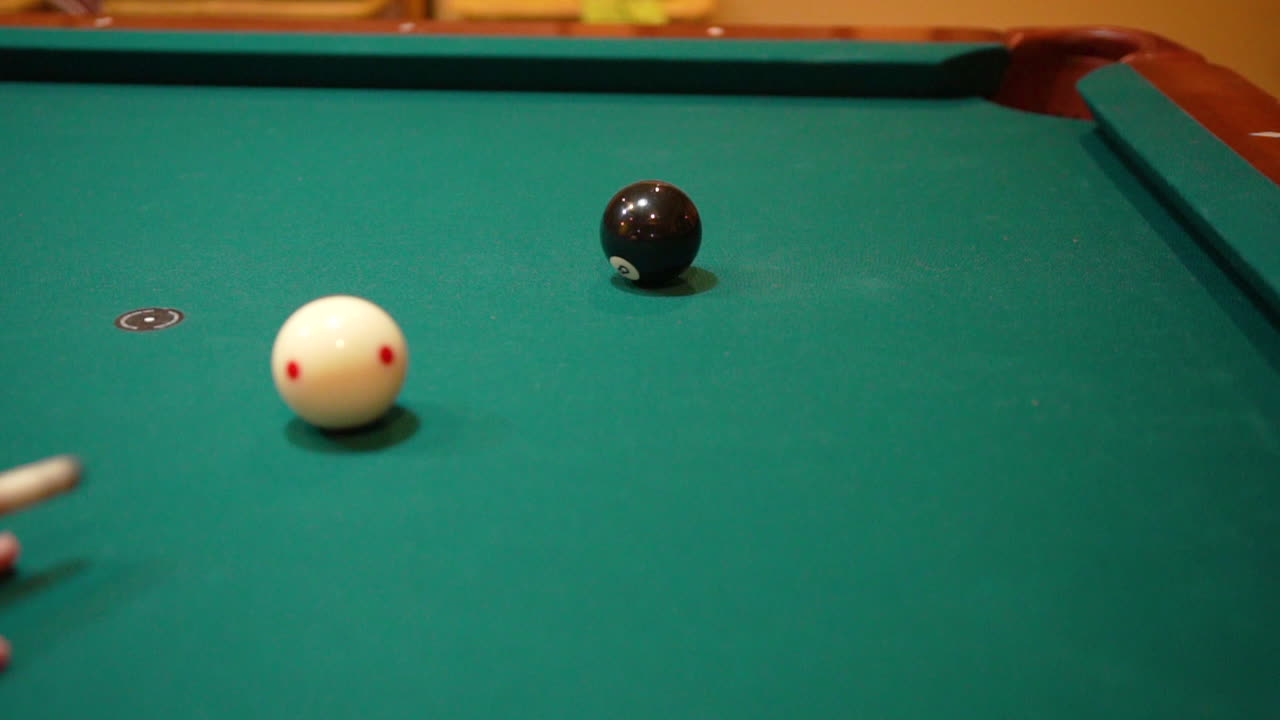 Slow Motion Billiards Person Shooting solid black 8 ball in corner pocket on a pool table with green felt using the cue ball and back spin or draw after practice strokes with cue stick Close Up