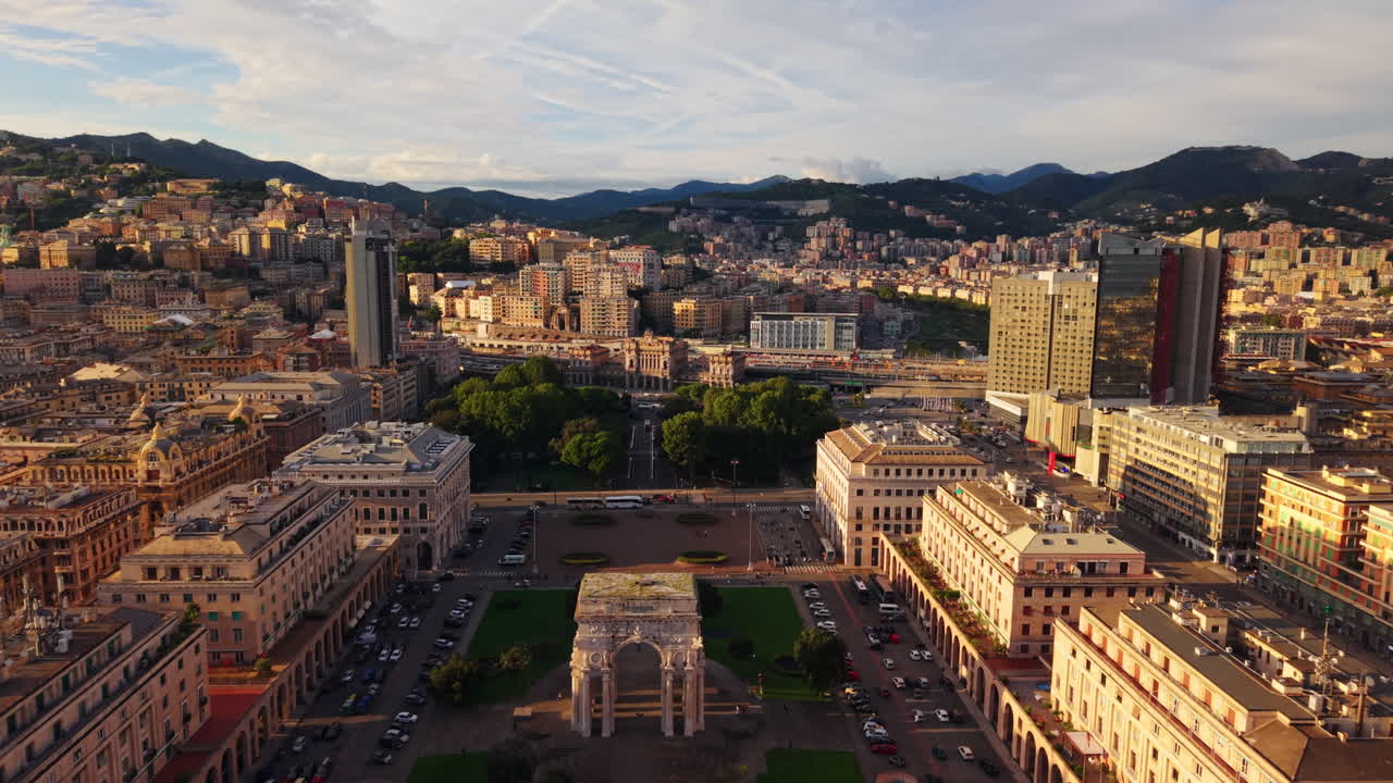Drone pulls back from Piazza della Vittoria revealing the arch, with the city and surrounding mountains in the background at sunset