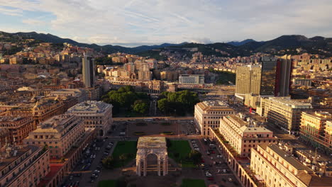drone pulls back from piazza della vittoria revealing the arch, with the city and surrounding mountains in the background at sunset